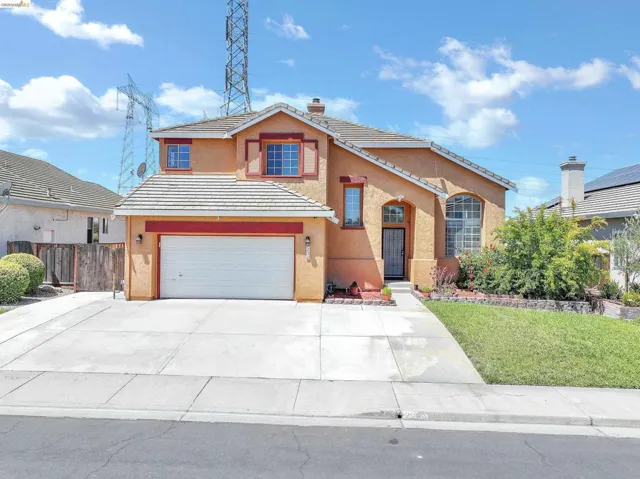 Stucco exterior featuring a two-car garage, concrete driveway, and front lawn with mature landscaping