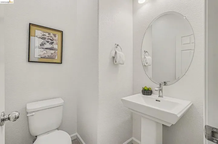 Pedestal sink with chrome faucet, oval mirror, and white toilet