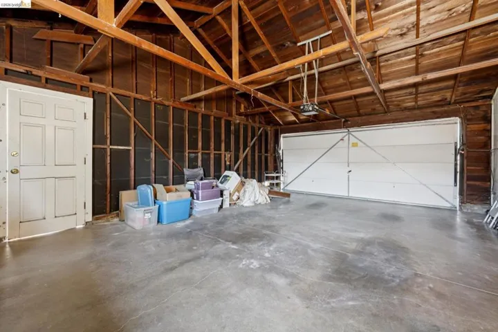 Spacious garage featuring exposed wood beam ceiling, concrete flooring, a paneled interior door, and a white two-car garage door