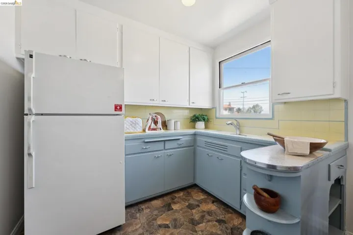 Kitchen featuring light blue lower cabinetry, white upper cabinetry, and a yellow tiled backsplash