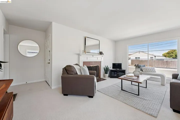 Bright living area featuring a prominent window, a detailed fireplace with a white mantel, and neutral-toned carpeting throughout
