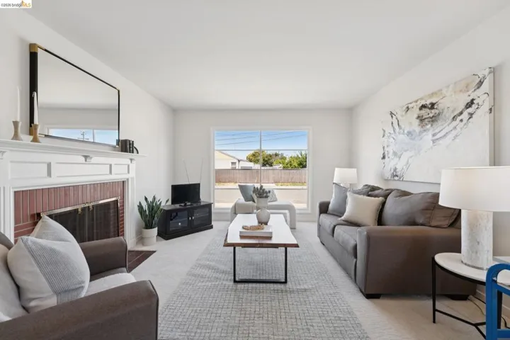 Bright living area featuring a white mantel fireplace with brick surround, wall-to-wall carpeting, and a large window providing outdoor light