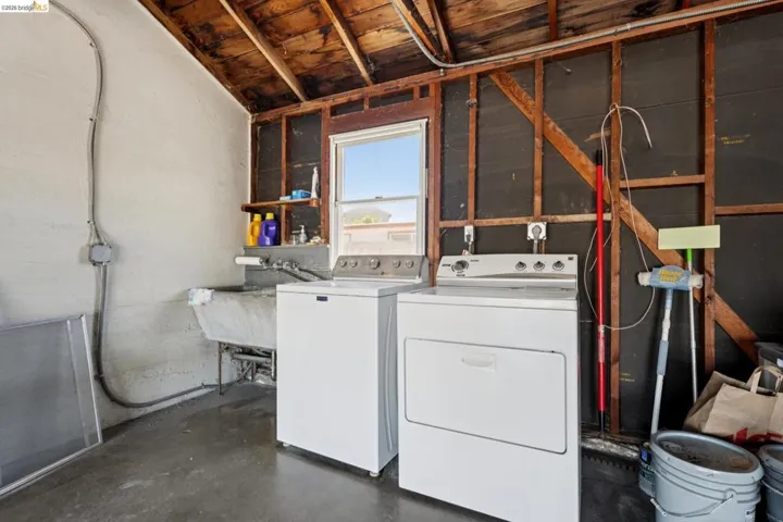 Dedicated laundry area featuring a utility sink, a window, and exposed wood ceiling joists