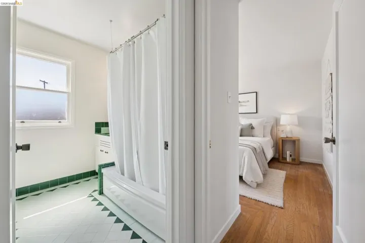 Bathroom featuring a white bathtub with a shower curtain, green tile trim, white tile flooring with green accents, and a window