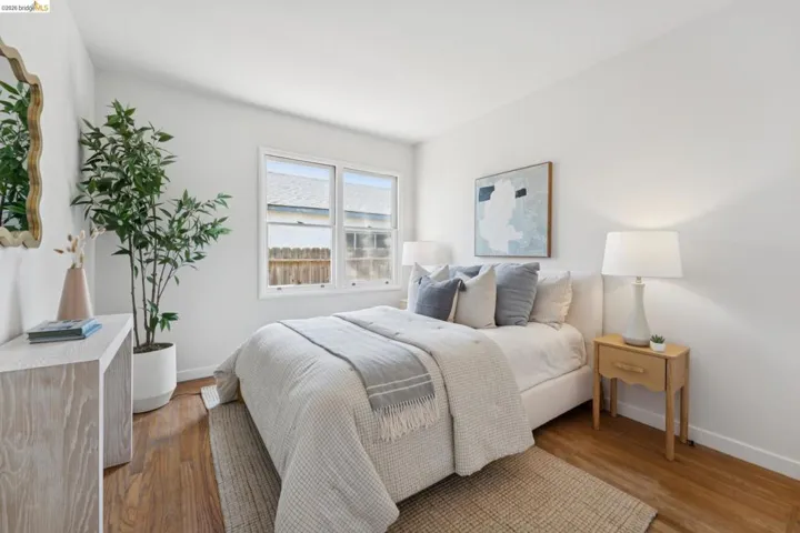Bright bedroom featuring wood-finish flooring, crisp white walls, and a large window providing natural light