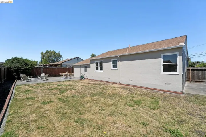 Expansive backyard featuring a concrete patio, wood fencing, and a stucco exterior