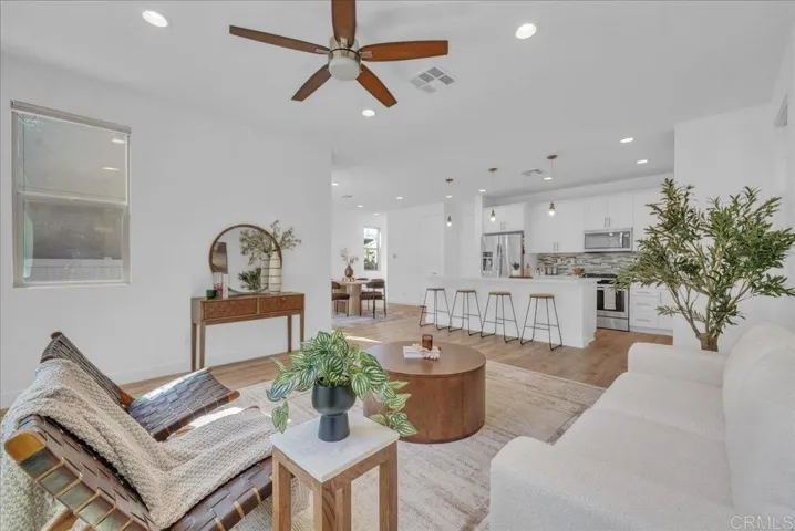 Open, inviting space with warm flooring, ceiling fan, and seamless flow to the kitchen.