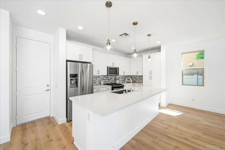 Open kitchen with quartz island, stainless appliances, and pendant lighting.