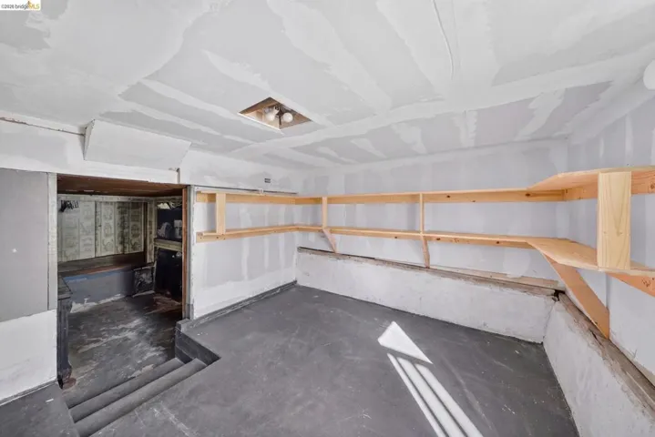 Room with concrete flooring and exposed drywall, featuring built-in wooden shelving along two walls