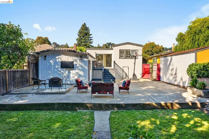 Rear exterior featuring a multi-level concrete patio, a detached structure with siding, and a basketball hoop