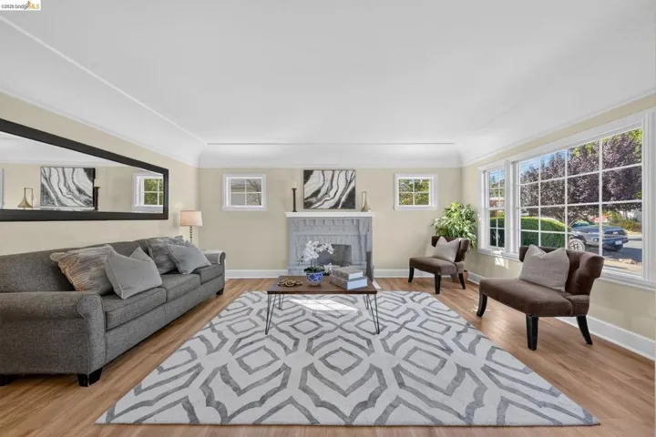Living space featuring wood-finish flooring, a decorative fireplace with a mantel, multiple windows, and crown molding