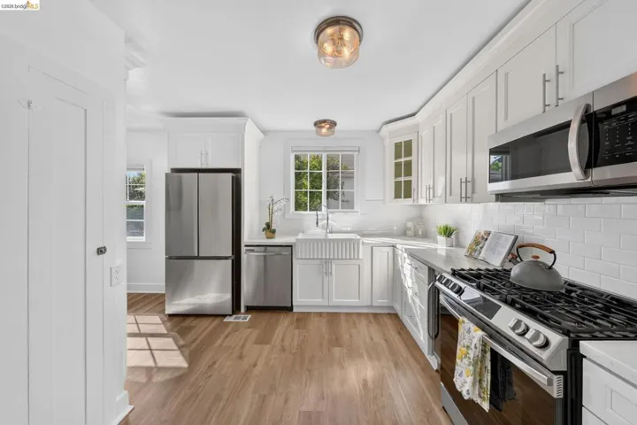 Modern kitchen featuring stainless steel appliances, white shaker cabinetry, wood-finish flooring, quartz countertops, and a subway tile backsplash
