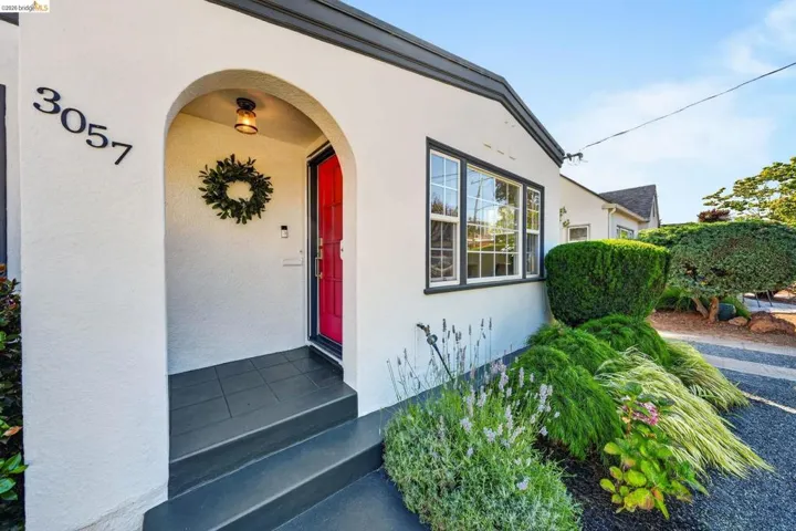 Stucco exterior featuring an arched entryway, vibrant red entry door, dark trim windows, and well-maintained landscaping with various plantings