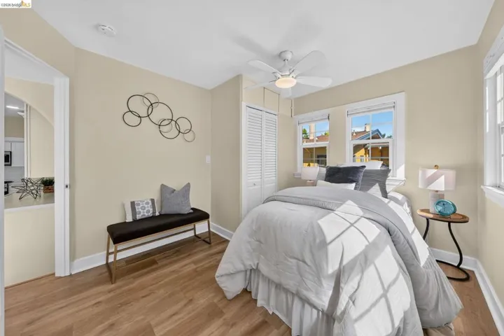 Bedroom featuring wood-finish flooring, multiple windows, a ceiling fan with light fixture, and white louvered closet doors