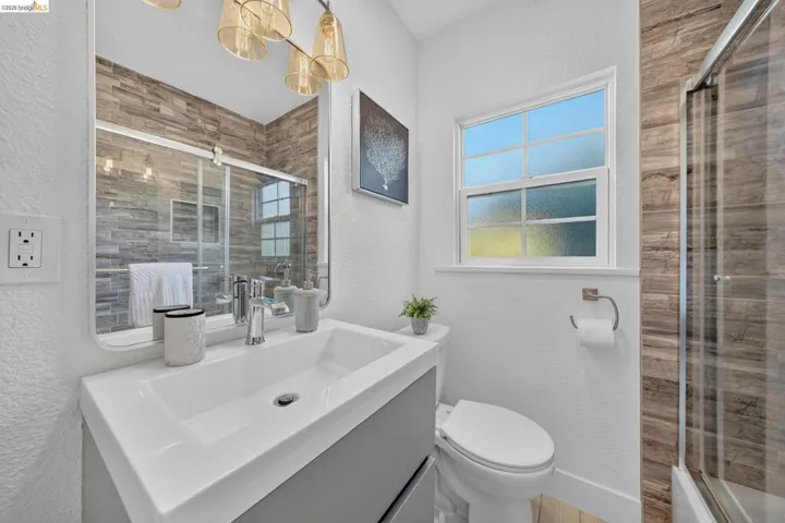 Contemporary bathroom featuring a white integrated sink vanity with matte gray cabinetry, a rectangular mirror, and a modern shower with a glass enclosure and wood-finish tile surround