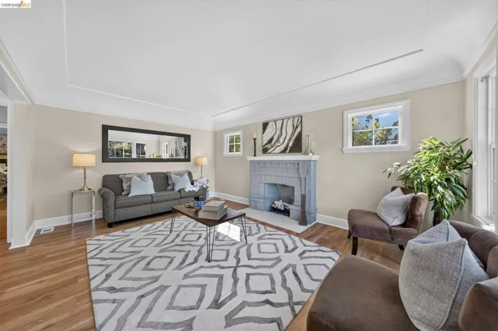 Living area featuring wood-finish flooring, a decorative fireplace with a stone surround, and multiple windows