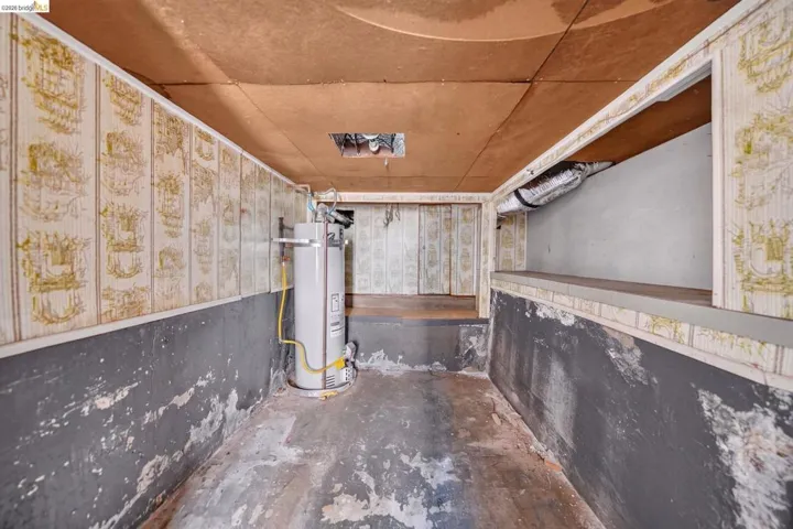 Utility area featuring a water heater, exposed ductwork, a multi-level concrete floor, and textured wall coverings