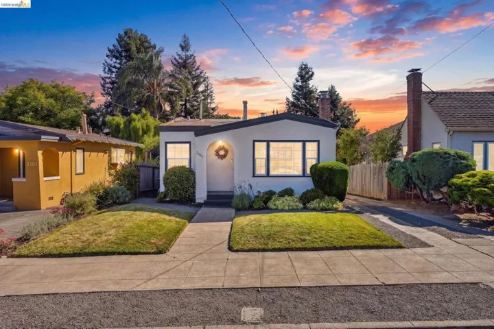 White stucco exterior with dark trim windows, a central arched entry, and a front lawn with established landscaping
