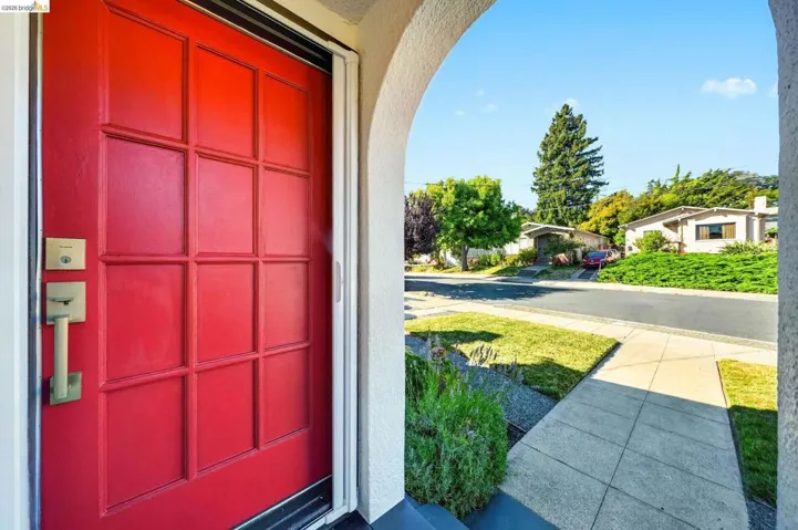 Red panel door with brass hardware and a screen door, framed by an arched entry