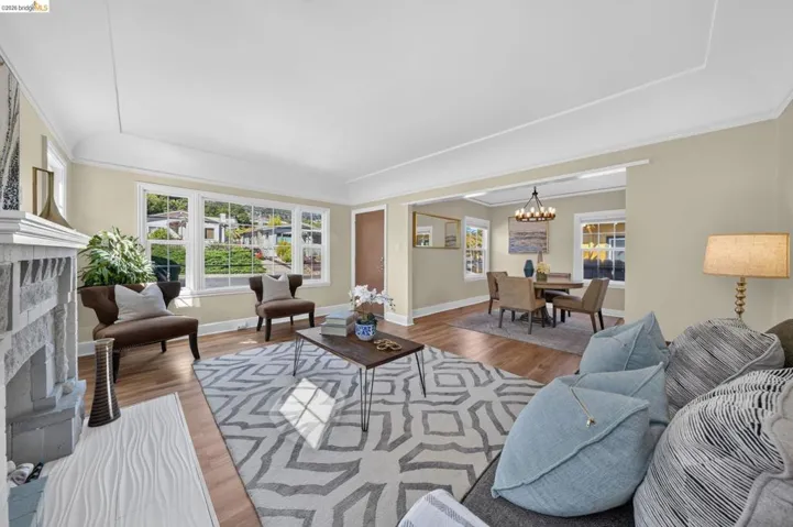 Spacious living area featuring wood-finish flooring, a stone fireplace, and multiple windows providing ample natural light