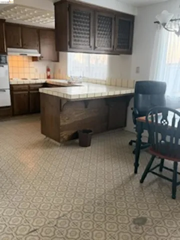 Kitchen featuring wood cabinetry with frosted glass inserts, tile countertops, and a tiled backsplash