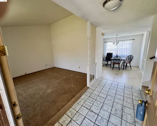 Entryway featuring square grid flooring, leading to a carpeted room and a dining area with patterned flooring