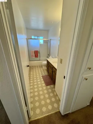 Bathroom featuring a wood-finish vanity with an integrated sink, patterned floor covering, and a window above the shower-tub combination