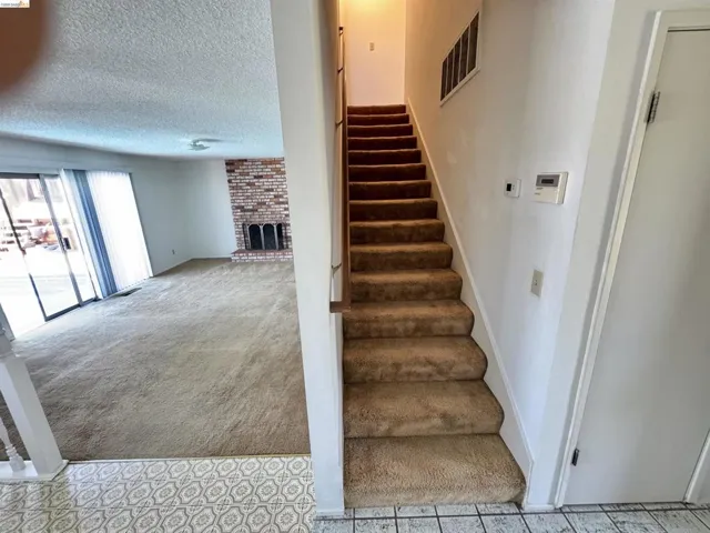 Staircase with carpeted treads and wood handrail, featuring a brick fireplace in the adjacent living area