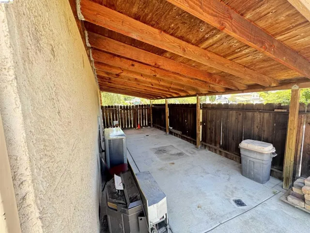 Covered outdoor patio with exposed wood beam ceiling, concrete flooring, and a perimeter wooden fence