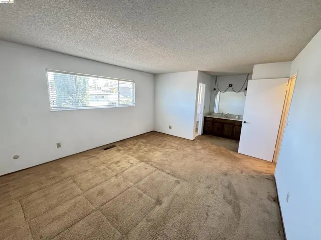 Spacious room featuring neutral carpet, a wide horizontal window with blinds, and white painted walls