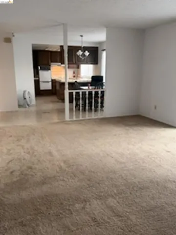 Broadloom carpeting spanning the foreground, leading to a kitchen area featuring dark wood cabinetry, a breakfast bar, and white built-in appliances
