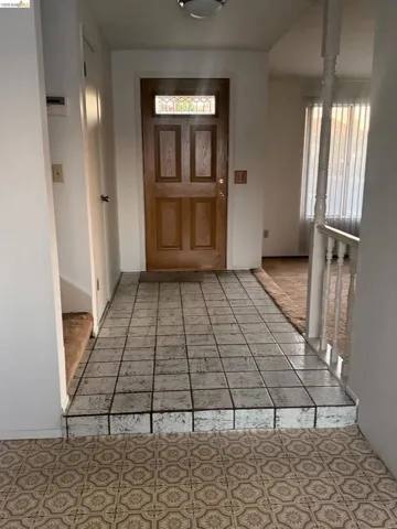 Wood-paneled front door with a decorative transom window, overhead flush-mount lighting, and square-tiled flooring