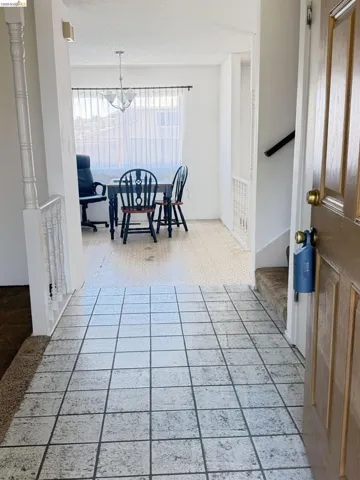 Entryway featuring light-toned square floor tiles, a natural wood-paneled door, and a white balustrade