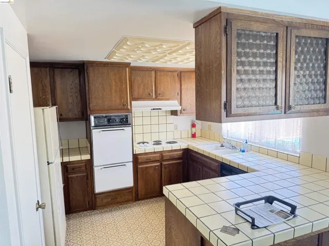 Kitchen featuring wood cabinetry, tile countertops, an integrated double oven, and built-in dishwasher