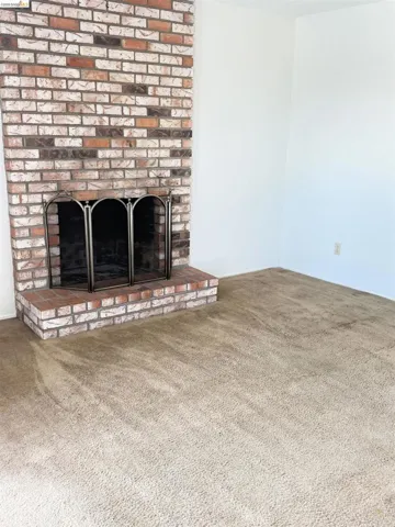 Brick fireplace with a metal fire screen, brick hearth, light-colored walls, and neutral carpeting