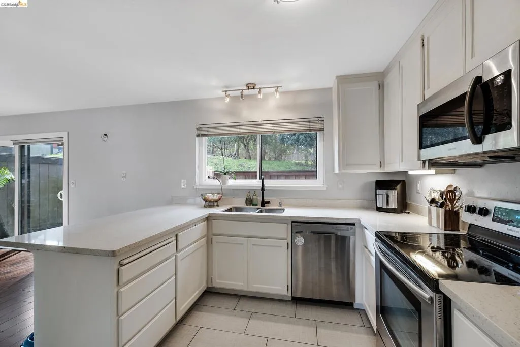 Kitchen with stainless steel appliances, white cabinets, a peninsula, and light stone counters
