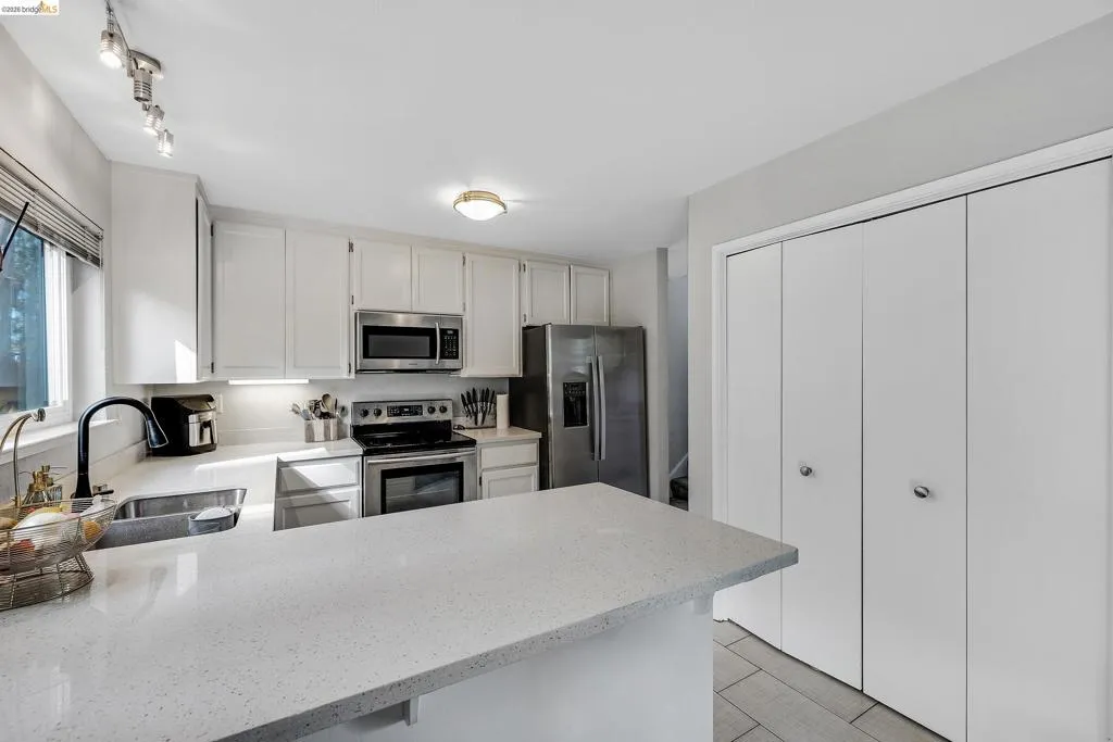 Kitchen featuring stainless steel appliances, white cabinetry, light stone countertops, and a peninsula