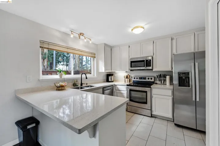 Kitchen featuring stainless steel appliances, a kitchen bar, a peninsula, light stone countertops, and white cabinetry