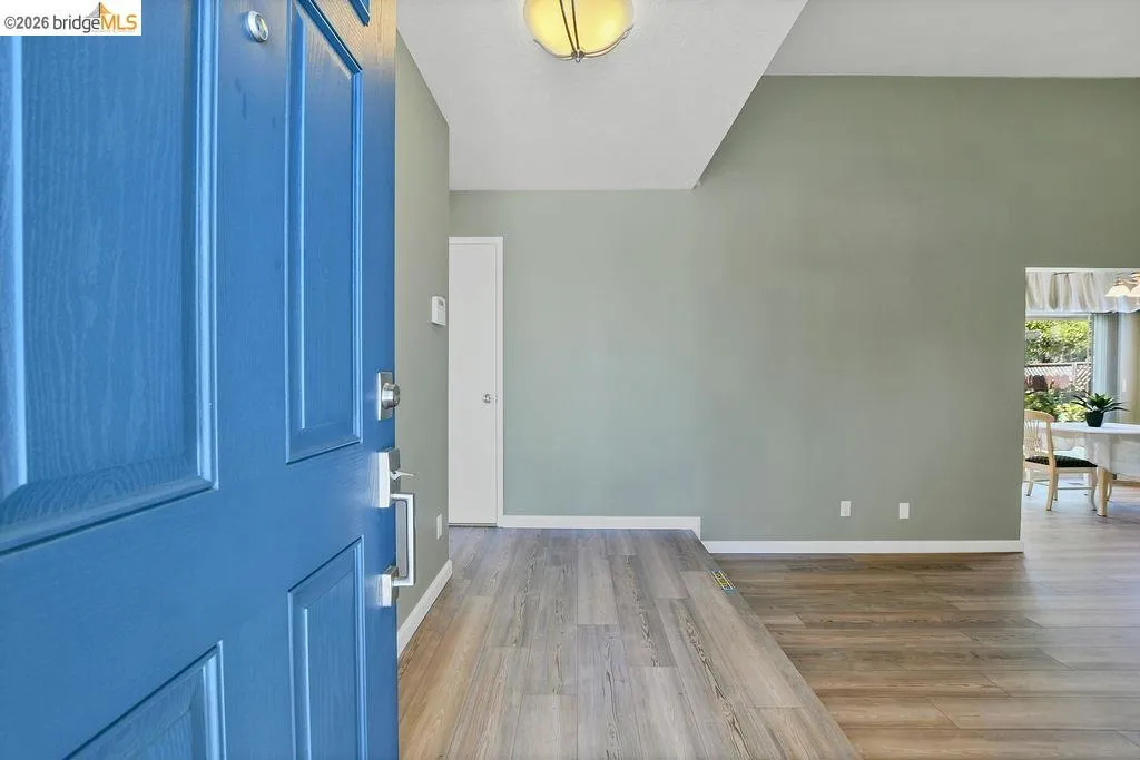 Vibrant blue front door opening to an interior featuring wood-finish flooring, vaulted ceilings, and light green walls