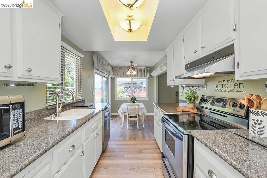 Galley kitchen featuring white cabinetry, stone-finish countertops, stainless steel appliances, and wood-finish flooring