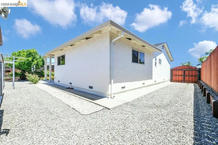 Exterior of property featuring white stucco siding, a gravel driveway, and a wood-tone privacy fence