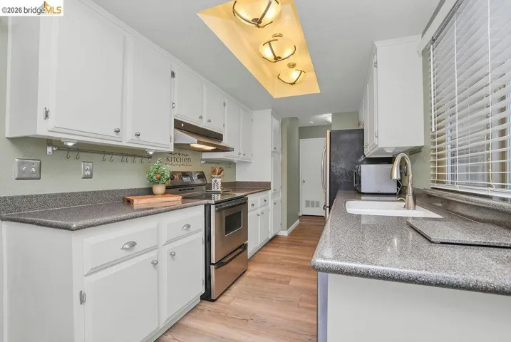 Galley kitchen featuring wood-finish flooring, white cabinetry, dark countertops, and stainless steel appliances