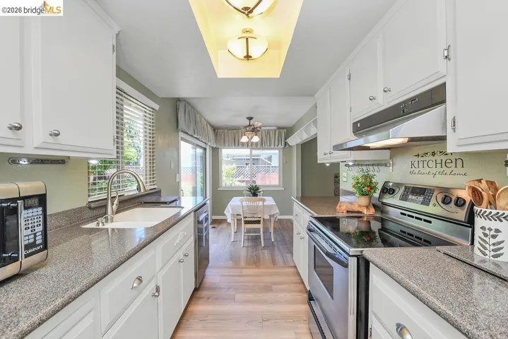 Galley kitchen featuring white cabinetry, stone-finish countertops, stainless steel appliances, and wood-finish flooring