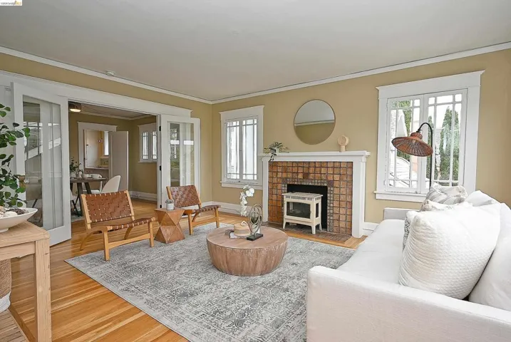 Living area with hardwood flooring, a tiled fireplace with white mantel, double French doors, and picture windows with white trim