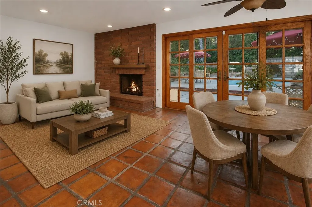 Photo is virtually staged.  Property shows as in previous photo. The family room is warmed by a floor-to-ceiling raised hearth brick fireplace and opens to the backyard through natural wood French doors, creating a seamless connection between indoor comfort and outdoor living.