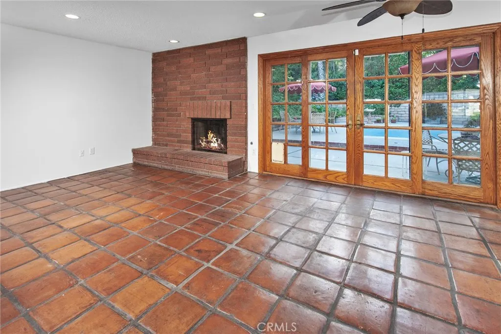 The family room is warmed by a floor-to-ceiling raised hearth brick fireplace and opens to the backyard through natural wood French doors, creating a seamless connection between indoor comfort and outdoor living.