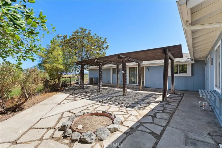 Back of the home with wooden covered patio and concrete inlay and a fire pit. There are also views to the west.