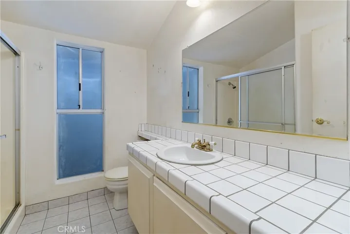 Hall bath with walk-in shower, tile counter and tile flooring.