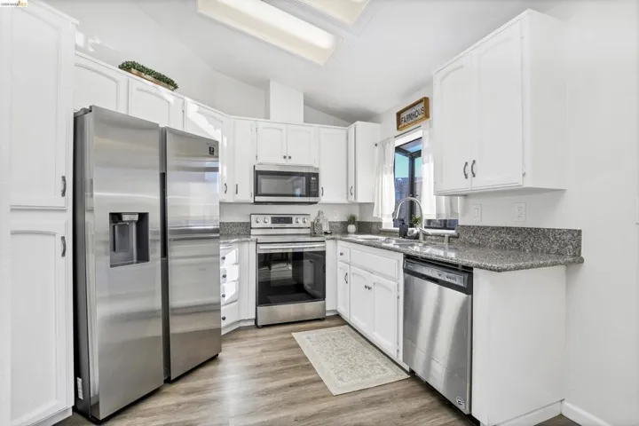 Kitchen featuring stainless steel appliances, white cabinetry, speckled countertops, and wood-finish flooring