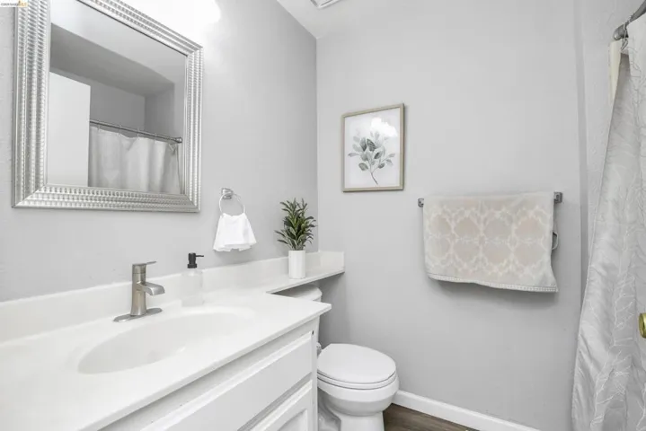 Bathroom featuring a white vanity with integrated sink, brushed nickel faucet, framed mirror, and wood-finish flooring